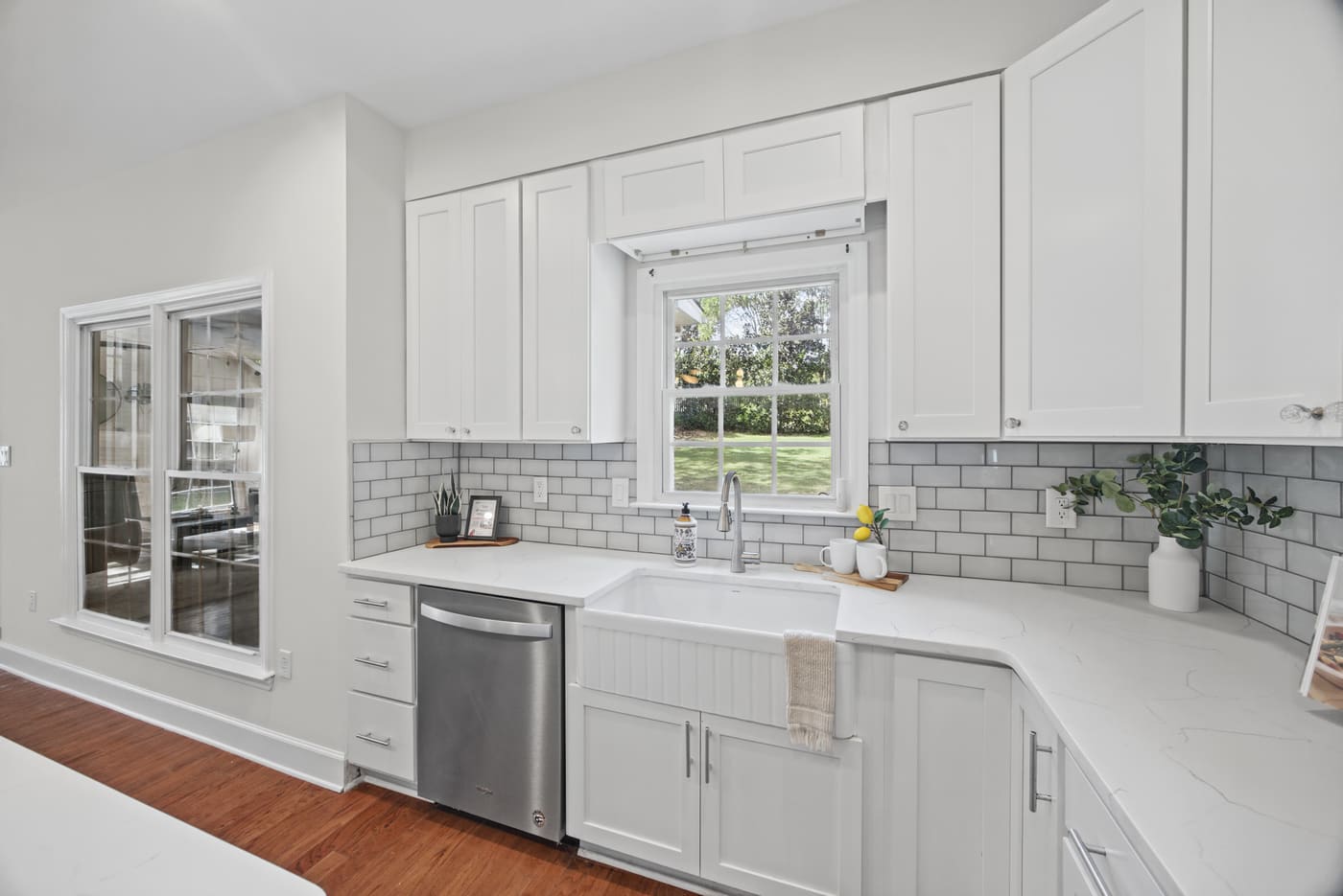 A farmhouse sink under the window, white subway tile, quartz counters and a stainless dishwasher.