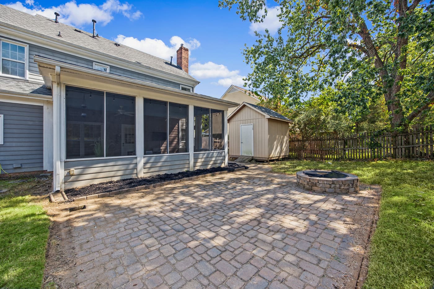 The back of the house with the screened porch, a paver patio, a stone firepit and a wood privacy fence.