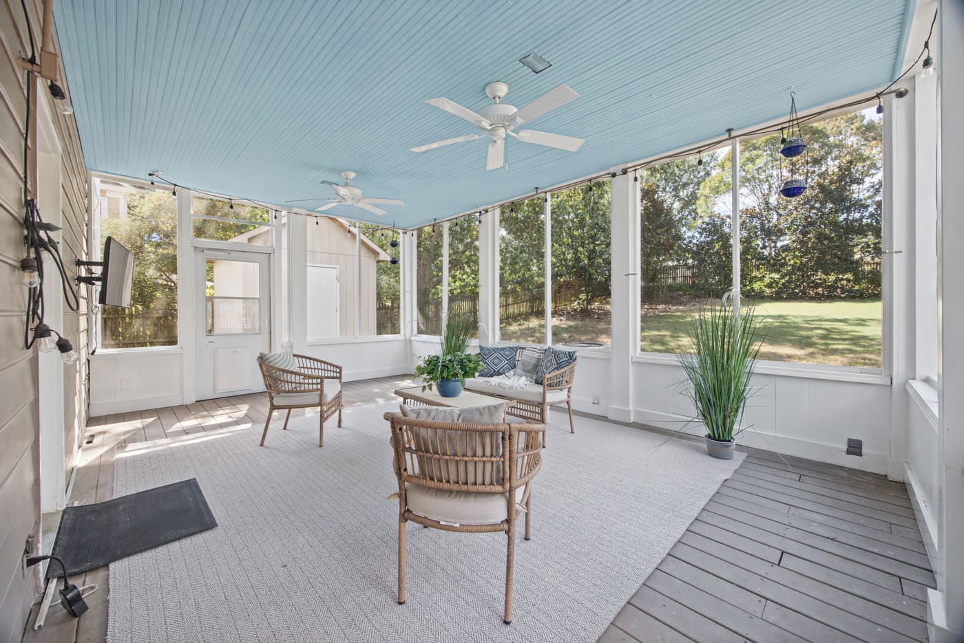 The screened rear porch with a pale blue ceiling, a ceiling fan and woven seating.